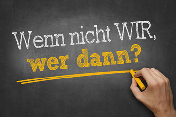 Hand schreibt mit Kreide Text "Wenn nicht wir, wer dann?" auf Tafel