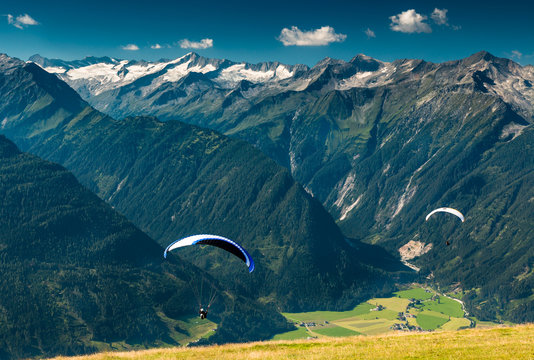two paraglides flying from wildkogel over the valley in austrian alps with glacier view