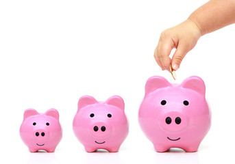 hand of a young baby giving golden coin to three piggy banks with different sizes