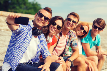 group of smiling friends with smartphone outdoors