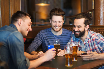 male friends with smartphones drinking beer at bar