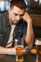 man with smartphone drinking beer at bar
