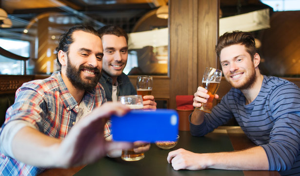 male friends with smartphone drinking beer at bar