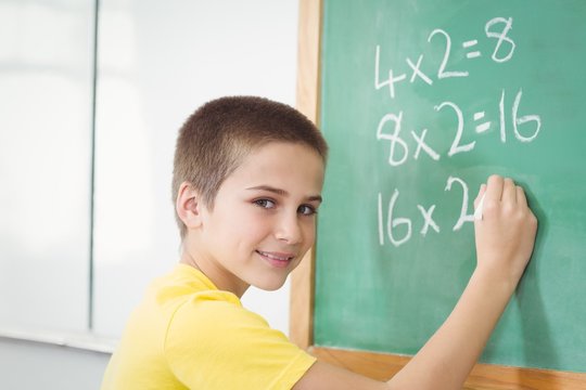 Smiling pupil calculating on chalkboard in a classroom