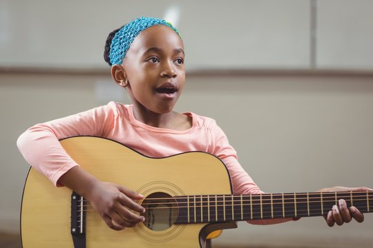 Cute pupil singing and playing guitar in a classroom