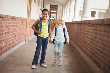 Smiling pupils holding hands at corridor