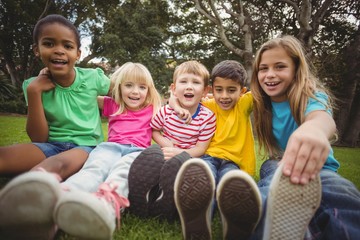 Happy classmates sitting in grass and having arms around