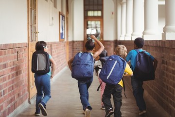 Rear view of happy pupils walking at corridor