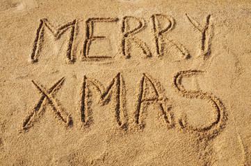 The words Merry Xmas written in the sand on the beach
