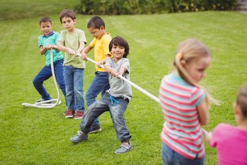 Fototapeta premium Cute pupils playing tug of war on the grass outside 