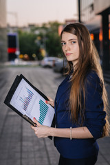 Successful smiling businessman, standing against the backdrop of buildings holding  folder with sales charts. City business woman working.