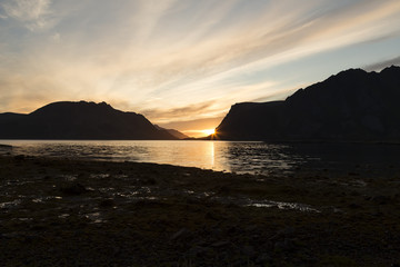 A setting sun behind some mountains in Lofoten with some water in the foreground