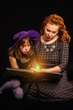 Young girl and mature mother at Halloween party reading magic book