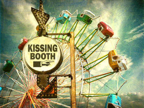 aged and worn vintage photo of kissing booth sign at carnival with ferris wheel in background