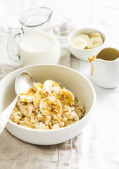 oatmeal with banana, caramel sauce and pecan nuts in a white bowl on a light surface, a delicious and healthy Breakfast