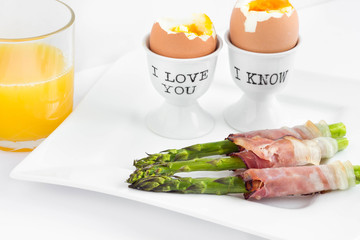 Asparagus wrapped in ham with boiled eggs and fresh orange juice.