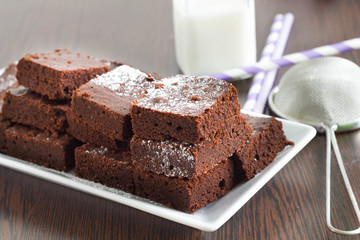 Brownies with a bottle of milk and colorful drinking straw on a kitchen table.