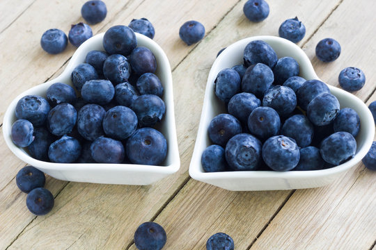 Two heart-shaped bowls full of healthy, fresh blueberries on a wooden table.
