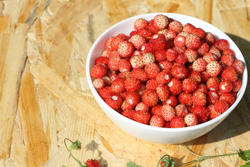 Ripe red wild strawberry in a plate on a wooden table outdoors