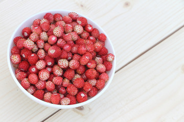 Ripe red wild strawberry in a plate on a wooden table outdoors