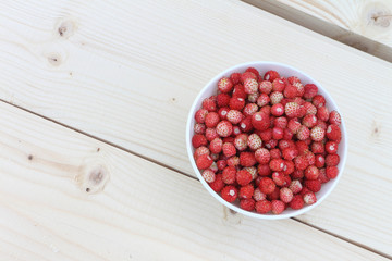 Ripe red wild strawberry in a plate on a wooden table outdoors