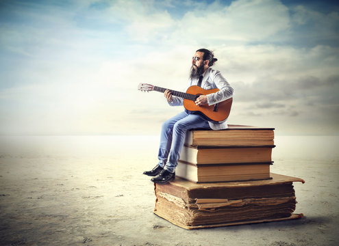 Man playing the guitar while sitting on a pile of books