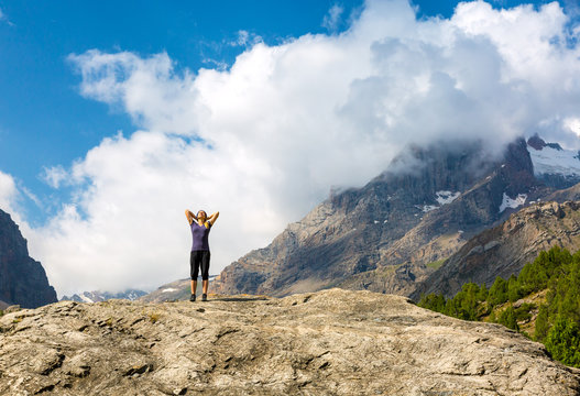 Young woman body on top of stone rock stretching body sunny morning mountain landscape background with arms raised up