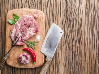 Raw pork steak with spices on the wooden cutting board.