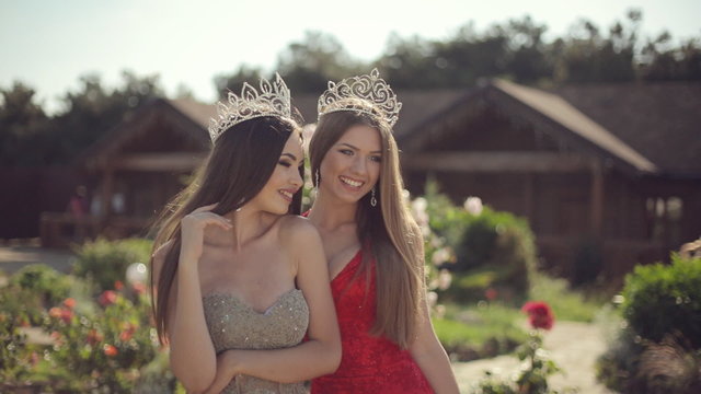 Two amazing girls in a long gowns and crowns laughing in the