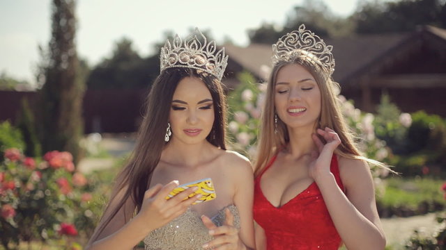 Two sexy young females in beautiful evening gowns and crowns