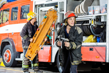 Alert Firefighter Holding Hose While Colleague Carrying Wooden S