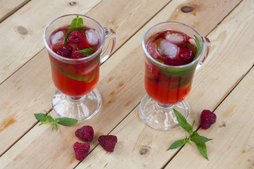 Raspberries fresh drinks with ice and mint on wooden table, selective focus