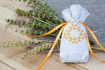 Sachet with ukrainian embroidery, sheaf of wheat and dried herbs on wooden background