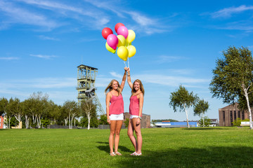 two pretty young women holding on to colourful balloons