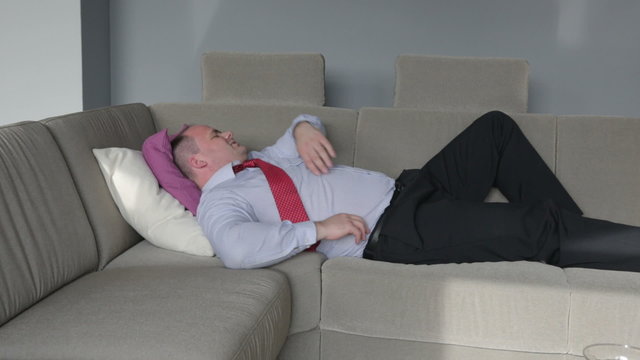 businessman lying on a couch in living room and having a headache 