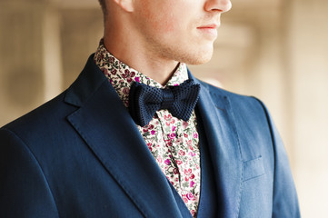 Dark blue bow tie with flowers shirt and suit on men's neck.