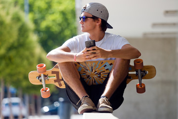 Handsome skater boy using his mobile phone in the street. - obrazy, fototapety, plakaty