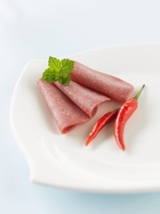 Three slices of salami with chillies on plate