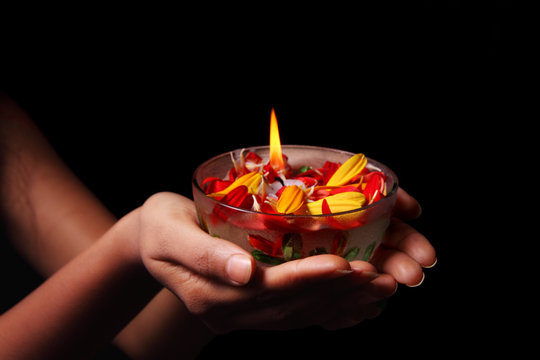 Hand holding a bowl containing flame and surrounded by red and yellow daisy flower petals