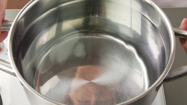 A gas cooked being turned on and a pot of water being placed upon it