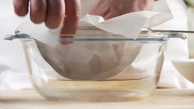 Broth being sieved through a sieve lined with kitchen paper