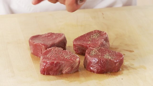Beef fillet slices being seasoned with pepper and salt
