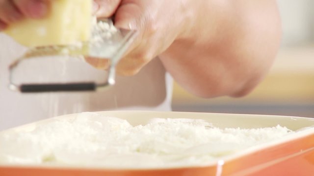 Lasagne being sprinkled with freshly grated Parmesan
