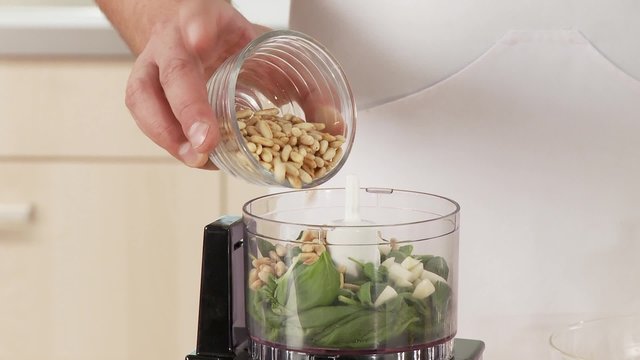 Pine nuts and grated cheese being added to pesto ingredients in a mixer