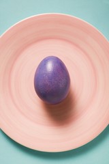 A purple Easter egg on a pink plate (seen from above)