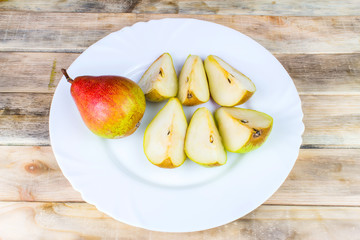 Sliced and whole pears in white plate, rustic wooden table