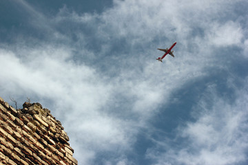 A plane in the blue cloudy sky leaves old city