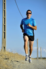 sport man with sun glasses running on countryside track with power line poles