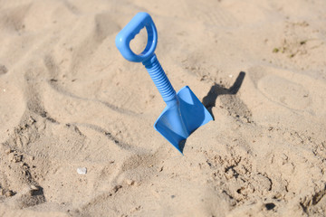 Fototapeta na wymiar blue beach shovel stuck in the sand by a child