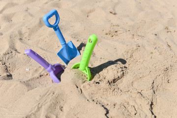 Fototapeta na wymiar blue, green and purple beach shovel stuck in the sand on a sunny